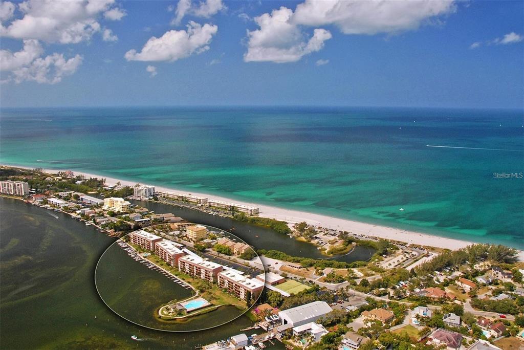 An aerial view shows a waterfront condominium complex with a pool on a narrow peninsula — 8911 MIDNIGHT PASS ROAD UNIT 514, SARASOTA, FL