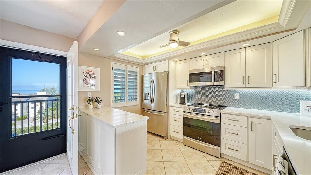 A kitchen with white cabinets, stainless steel appliances, and a view of the ocean outside — 8911 MIDNIGHT PASS ROAD UNIT 514, SARASOTA, FL