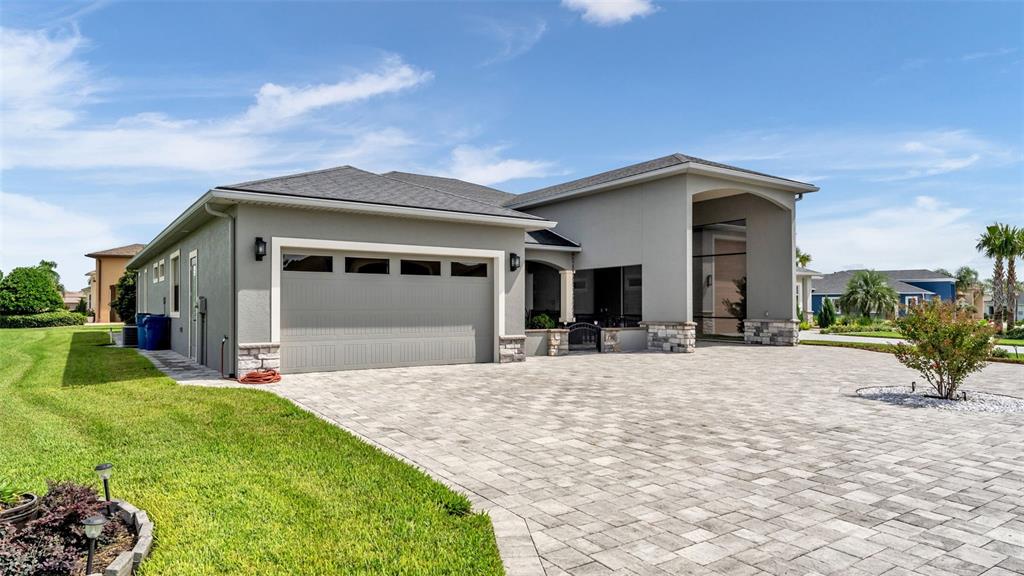 A gray house with a stone-accented garage and a large paved driveway under a sky — 790 TEABERRY TRAIL, POLK CITY, FL