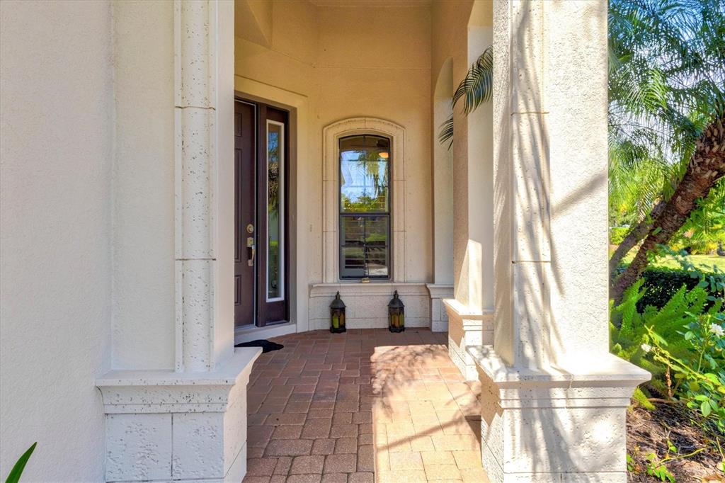 A covered entryway features a brick paver floor, two stone columns, and a dark front door — 7118 WESTHILL COURT, BRADENTON, FL