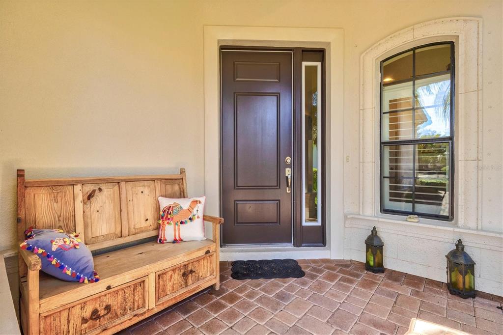 A wooden bench with decorative pillows sits on a brick porch beside a front door — 7118 WESTHILL COURT, BRADENTON, FL