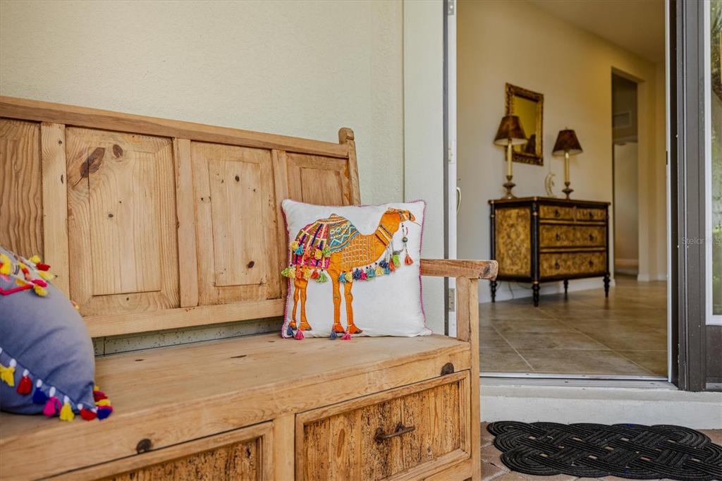 A wooden bench with decorative pillows sits on a patio outside a sliding glass door — 7118 WESTHILL COURT, BRADENTON, FL