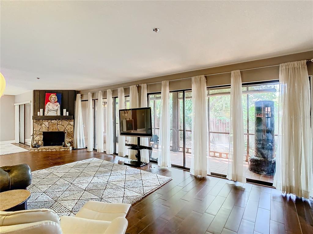 A living room with hardwood floors, a stone fireplace, and floor-to-ceiling windows overlooking a patio — 976 E MICHIGAN STREET UNIT A, ORLANDO, FL