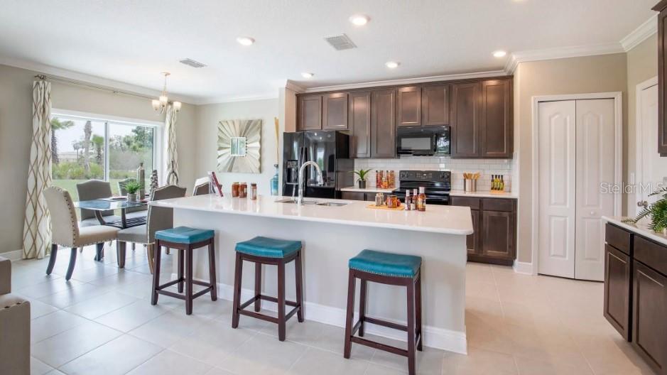 A kitchen features dark wood cabinets, a white island with teal stools, and dining area — 1465 TRINIDAD STREET, DELAND, FL