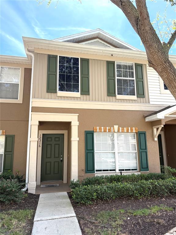 A two-story townhouse exterior features tan stucco, vertical siding, green shutters, and a front walkway — 12316 HEALEY SUMMIT LANE, RIVERVIEW, FL