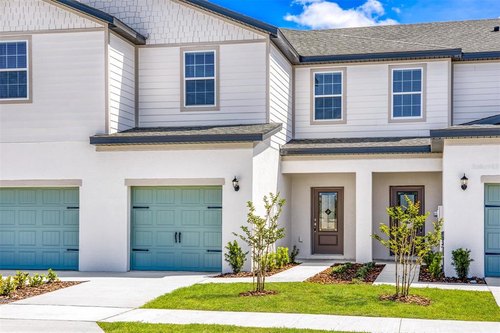 The exterior of a two-story townhouse features white siding, light blue garage doors, and entryways — 672 POPPY LANE, DUNDEE, FL