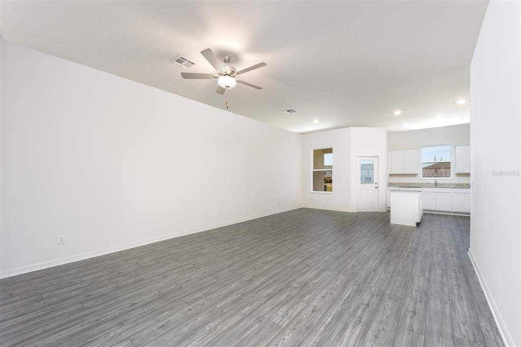 An open-concept living area features gray wood-look flooring, white walls, and a kitchen with white cabinetry — 672 POPPY LANE, DUNDEE, FL