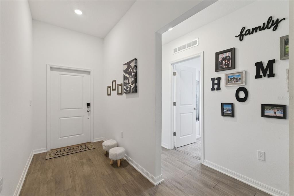 A bright entryway features white walls, wood-look flooring, a front door, and a gallery wall — 3963 WILLOWBROOK DRIVE, EDGEWATER, FL
