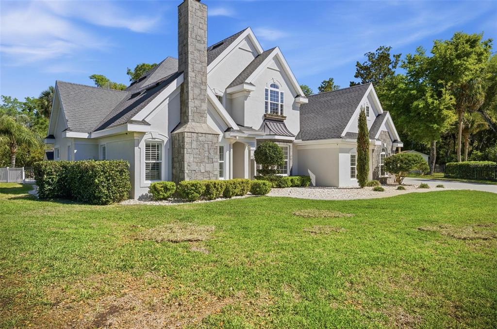 A two-story house with a stone chimney, gray shingled roof, and a green lawn — 4105 PIUTE LANE, ORMOND BEACH, FL