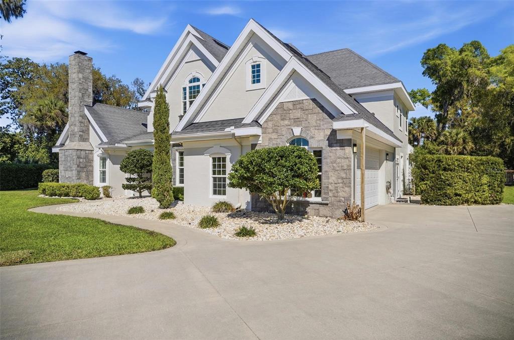 A two-story house with a stone chimney, stucco siding, and a large concrete driveway — 4105 PIUTE LANE, ORMOND BEACH, FL
