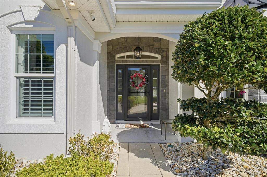 The front entrance features a glass storm door, stone facade, and a manicured topiary tree — 4105 PIUTE LANE, ORMOND BEACH, FL