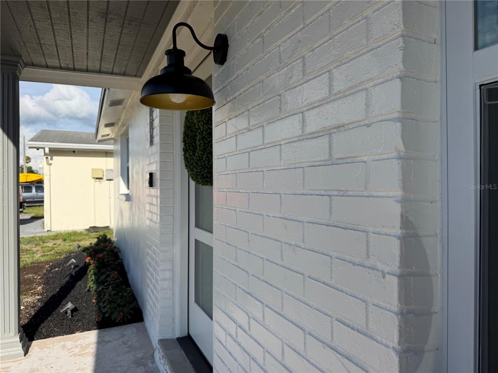A white painted brick exterior wall features a black gooseneck light fixture near the entrance — 7220 FOX HOLLOW DRIVE, PORT RICHEY, FL