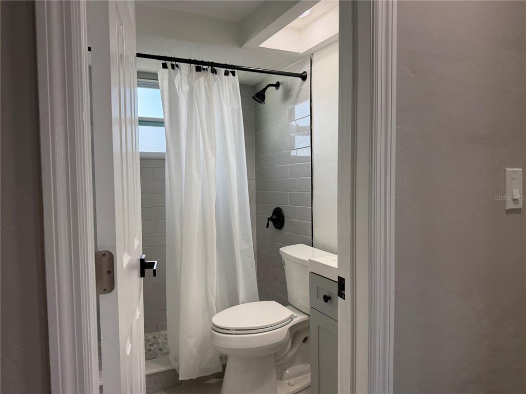 A bathroom features a toilet, a vanity, and a shower with gray subway tile walls — 7220 FOX HOLLOW DRIVE, PORT RICHEY, FL
