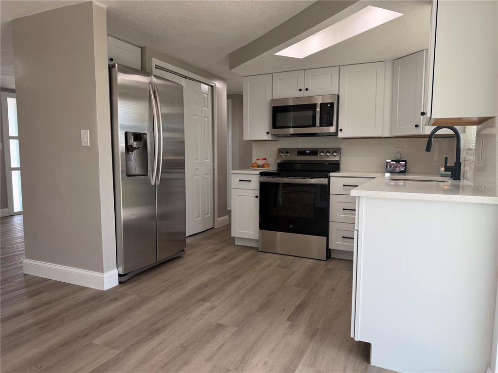 A kitchen features white cabinets, stainless steel appliances, and light wood-look flooring — 7220 FOX HOLLOW DRIVE, PORT RICHEY, FL
