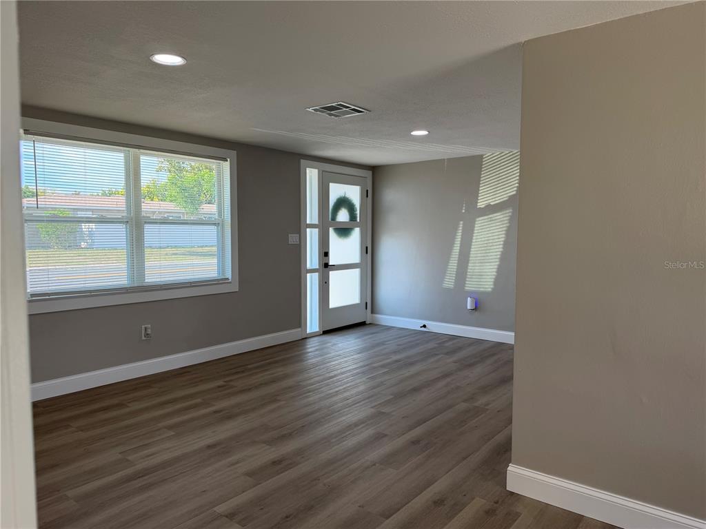 A living room features light wood-look flooring, gray walls, recessed lighting, and a modern front door — 7220 FOX HOLLOW DRIVE, PORT RICHEY, FL