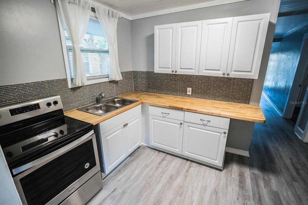 A kitchen features white cabinets, a wood countertop, a stainless steel stove, and gray flooring — 2625 4TH AVENUE S, ST PETERSBURG, FL