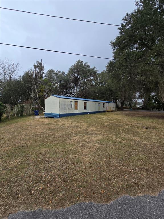 A long, single-wide mobile home sits on a grassy lot surrounded by mature trees — 20 SW 3RD STREET, WEBSTER, FL