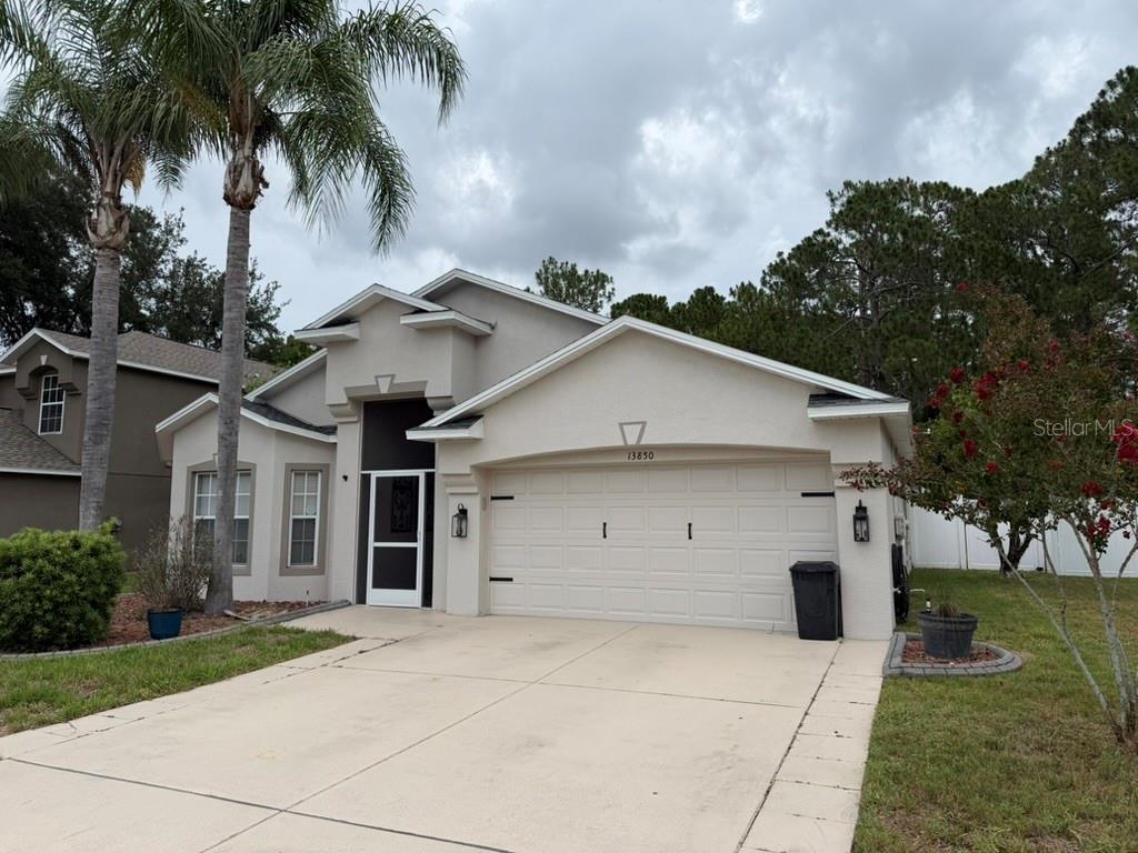 A single-story suburban house with a beige stucco exterior, a two-car garage, and palm trees — 13850 ROYSTON BEND, HUDSON, FL