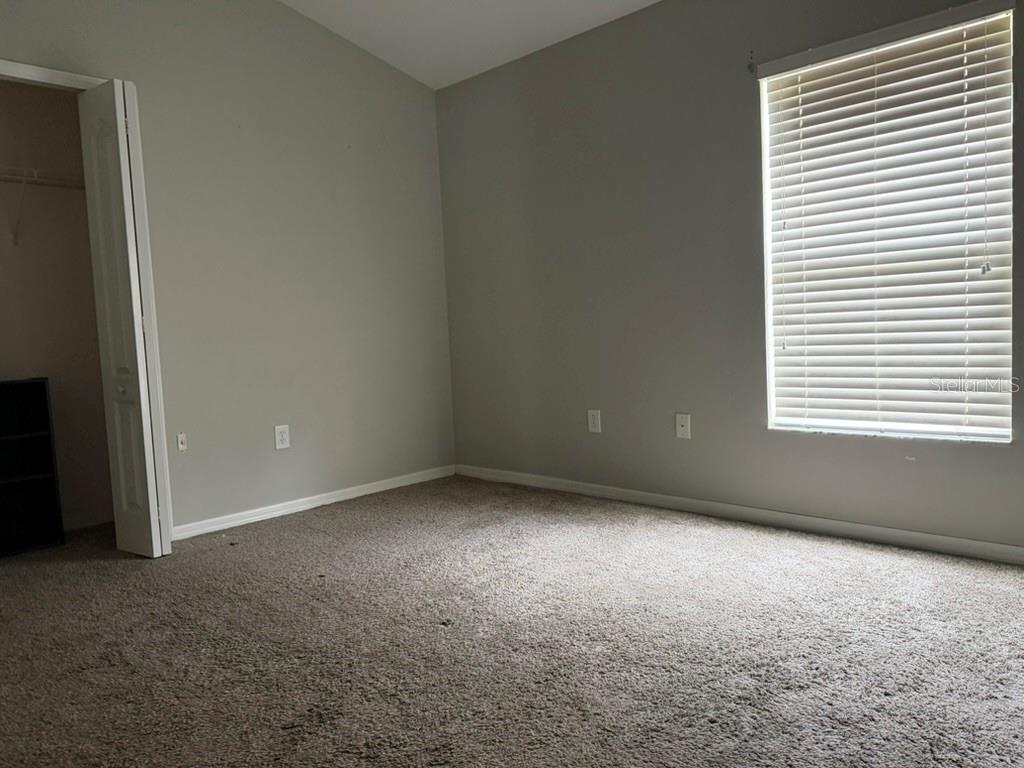 An empty bedroom features beige carpet, light gray walls, a closet, and a window with blinds — 13850 ROYSTON BEND, HUDSON, FL