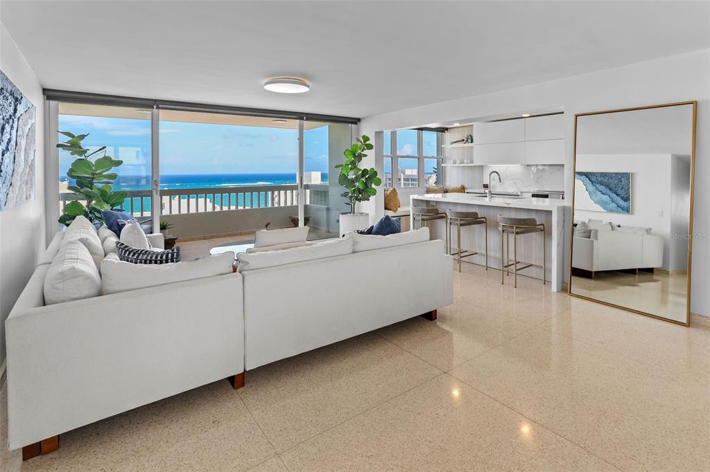 A modern living room and kitchen area with a white sectional sofa and ocean view — 70 KINGS COURT UNIT 17C, SAN JUAN, PR