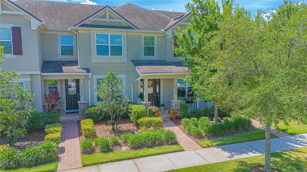 An exterior view of two adjacent townhomes with brick walkways, manicured landscaping, and green lawns — 10520 BURROWS STREET, ORLANDO, FL