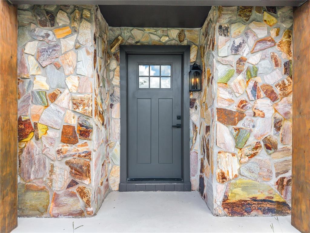 A dark gray front door is framed by natural stone walls and a concrete porch — 8624 BAYLOR CIRCLE, ORLANDO, FL