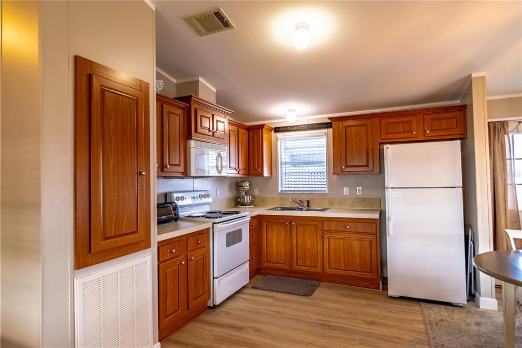 A kitchen with wood cabinets, white appliances, and light wood-look flooring — 8320 RIVERSIDE DRIVE UNIT 51B, PUNTA GORDA, FL