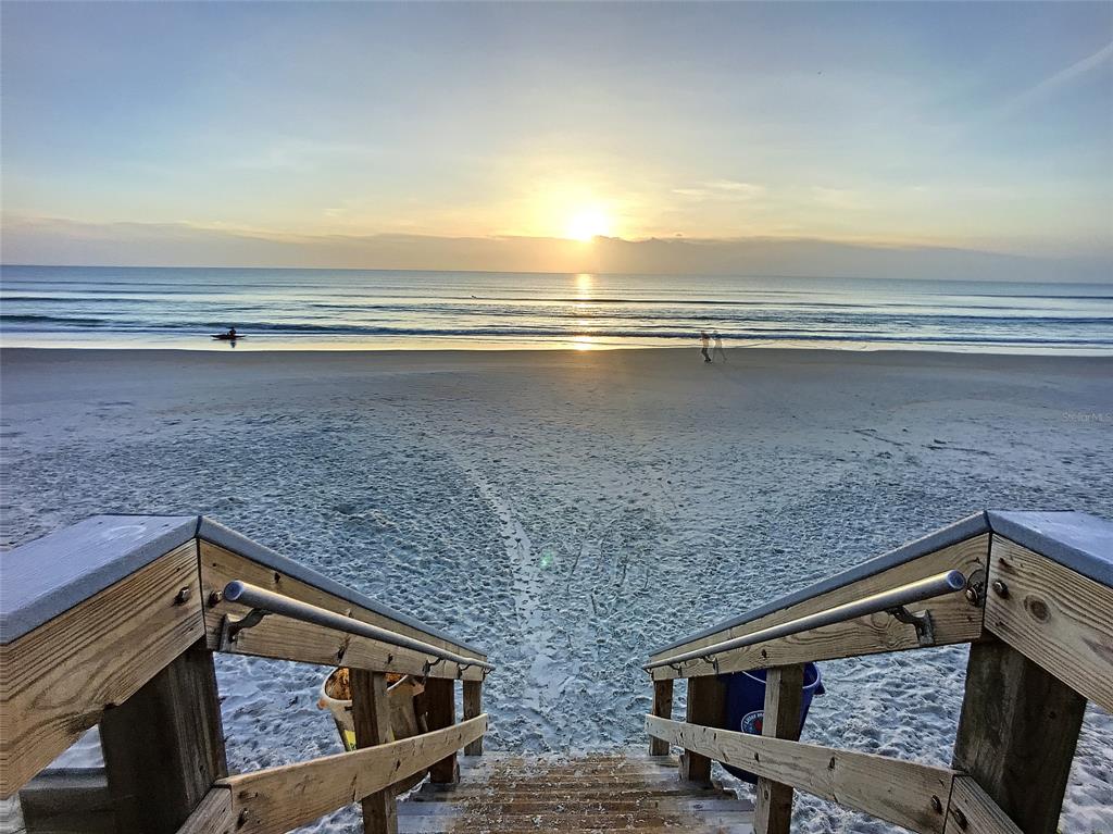 A wooden staircase leads down to a sandy beach at sunrise with the ocean ahead — 4148 MICHIGAN AVENUE, NEW SMYRNA BEACH, FL
