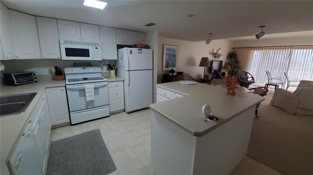 A kitchen with white cabinets and white appliances opens into a living area with carpet — 815 OCEAN SHORE BOULEVARD UNIT 6B, ORMOND BEACH, FL