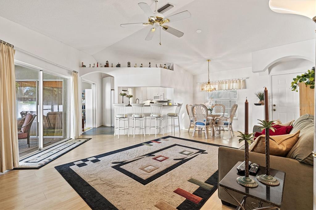 A living and dining area with a ceiling fan, light wood floors, and a breakfast bar — 5128 18TH LANE E, BRADENTON, FL