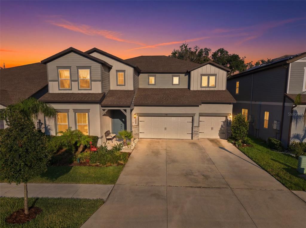 A two-story suburban house with a three-car garage and a concrete driveway at sunset — 11481 OWASEE TRAILS PLACE, RIVERVIEW, FL