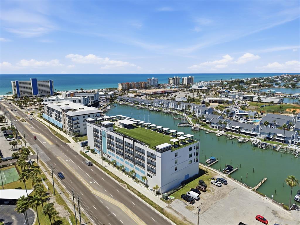 An aerial view shows a modern building with a rooftop terrace beside a coastal waterway — 400 150TH AVENUE UNIT 305, MADEIRA BEACH, FL