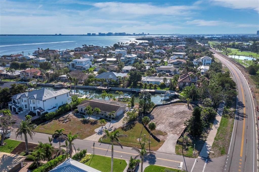 An aerial view shows a coastal neighborhood with a vacant lot, houses, and a canal — 500 OUTRIGGER LANE, LONGBOAT KEY, FL