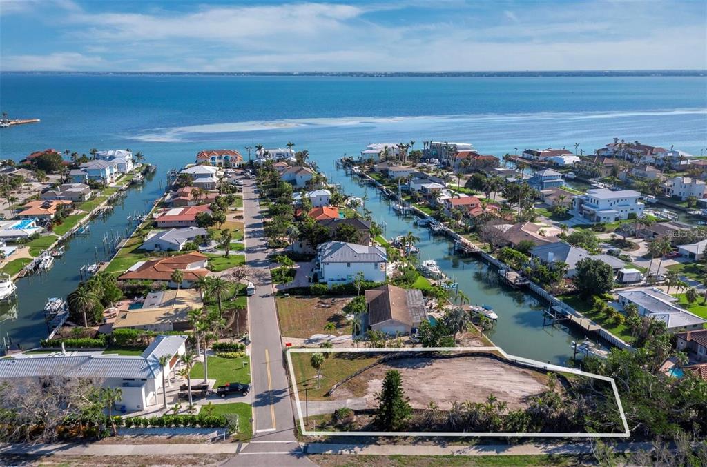 An aerial view shows a vacant waterfront lot outlined in white next to a residential street — 500 OUTRIGGER LANE, LONGBOAT KEY, FL
