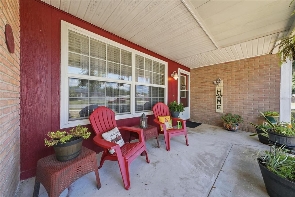 A covered front porch features red siding, brick walls, two red chairs, and potted plants — 3801 UPLAND PLACE, VALRICO, FL