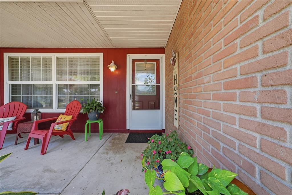 A covered front porch features a brick wall, red siding, and two red Adirondack chairs — 3801 UPLAND PLACE, VALRICO, FL