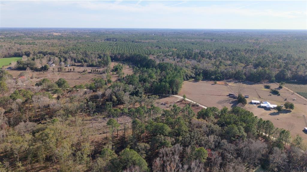 An aerial view shows a rural landscape with wooded areas, open fields, and a small farmhouse — 14403 NW 258TH PLACE, ALACHUA, FL