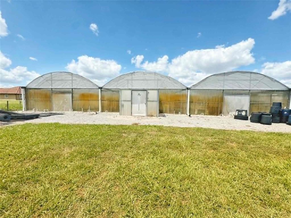 A exterior view of three connected greenhouses with arched roofs and a central door — 612 MORGAN ROAD, WINTER HAVEN, FL