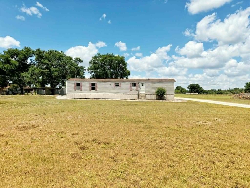 A single-story mobile home sits on a large, grassy lot under a blue sky — 612 MORGAN ROAD, WINTER HAVEN, FL