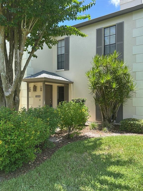 The exterior of a two-story townhouse features a covered entryway, gray shutters, and landscaping — 13046 VILLAGE CHASE CIRCLE UNIT 13046, TAMPA, FL