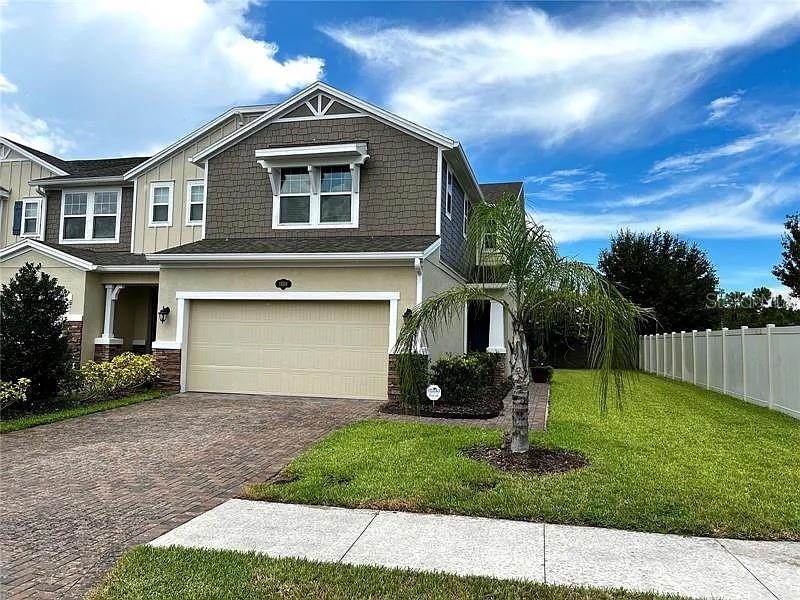A two-story suburban house features a tan stucco exterior, a brick driveway, and a palm tree — 18814 CORNUTA STREET, LUTZ, FL