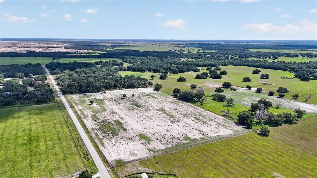An aerial view shows a large, cleared rectangular lot bordered by a road and trees — CR 665, ONA, FL