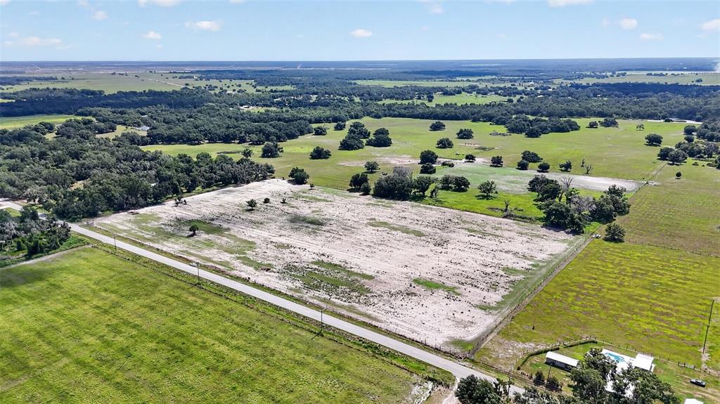An aerial view shows a large, cleared sandy lot bordered by a road and trees — CR 665, ONA, FL