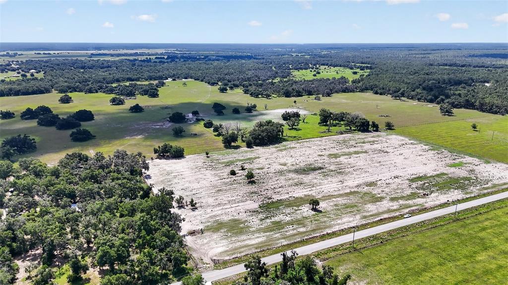 An aerial view shows a large, cleared sandy lot bordered by trees and a road — CR 665, ONA, FL