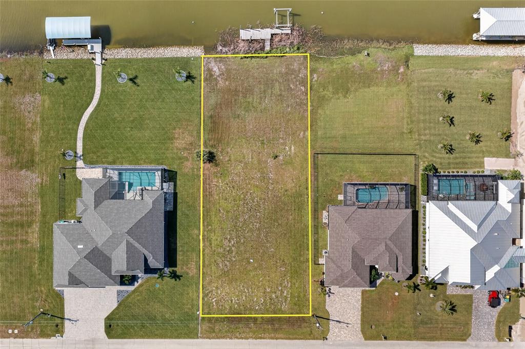 An aerial view shows a vacant rectangular waterfront lot situated between two residential homes — 16652 LIGGETT CIRCLE, PORT CHARLOTTE, FL