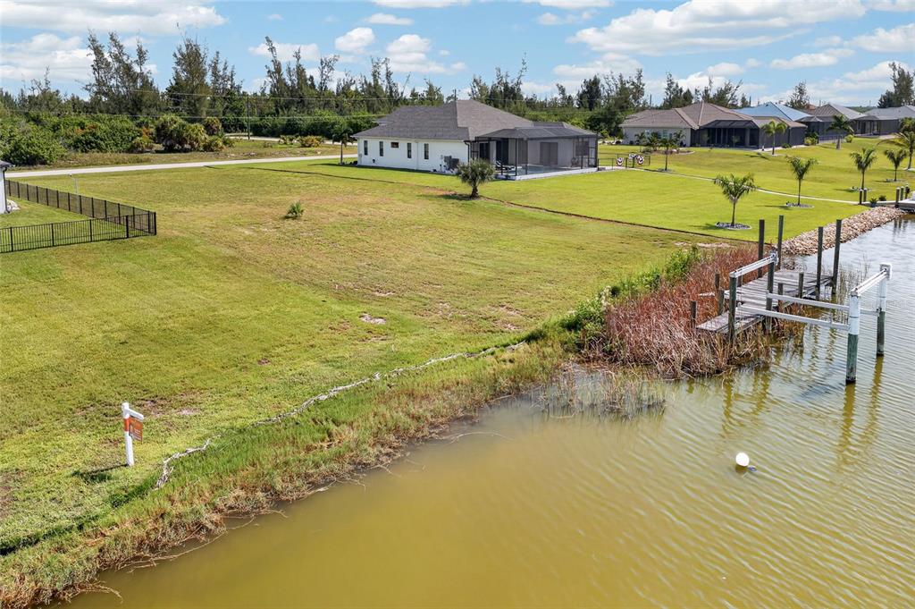 An aerial view shows a vacant waterfront lot with a dock next to a house — 16652 LIGGETT CIRCLE, PORT CHARLOTTE, FL