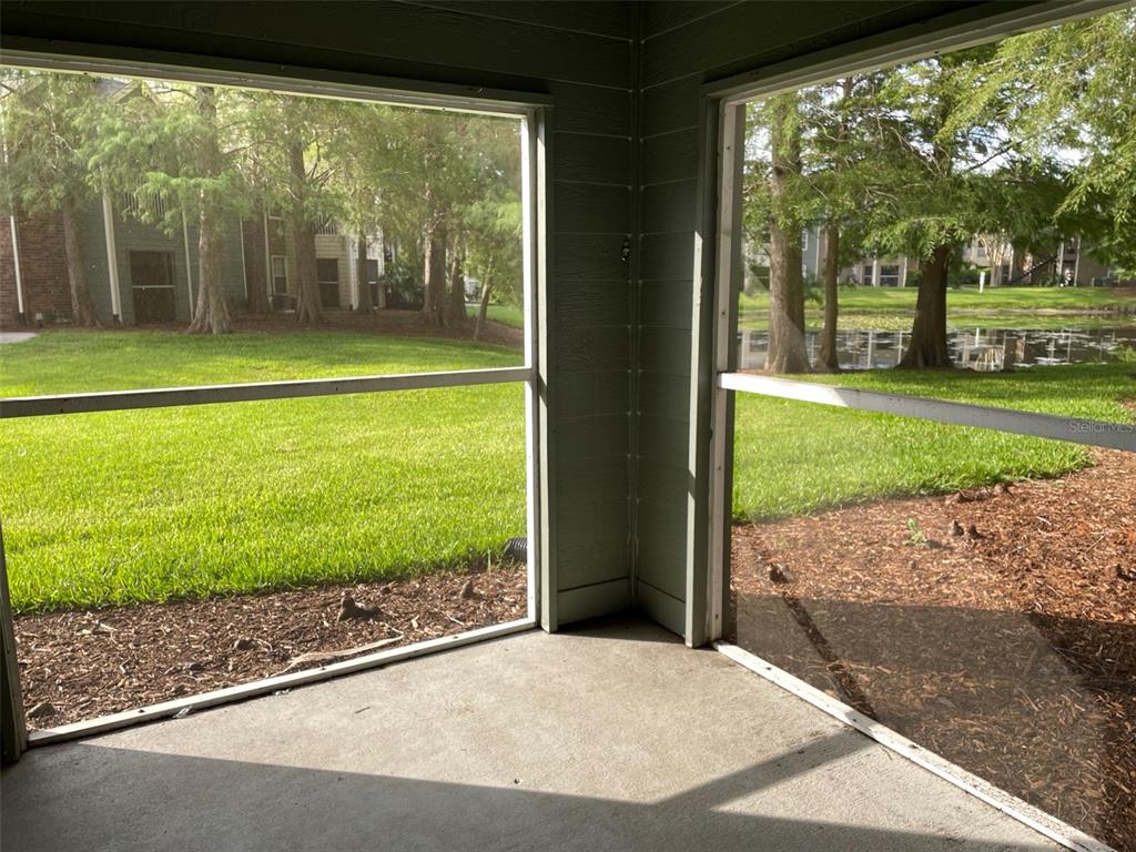 A screened-in porch with concrete flooring overlooks a grassy lawn and a pond — 2225 METROPOLITAN WAY UNIT 1218, ORLANDO, FL