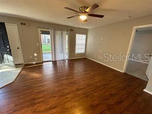 An empty living room features wood-look flooring, a ceiling fan, and sliding glass patio doors — 2225 METROPOLITAN WAY UNIT 1218, ORLANDO, FL