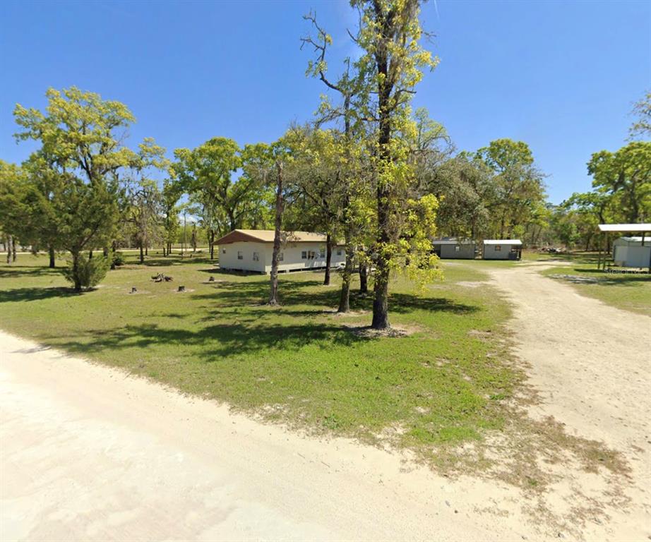 A single-story house sits on a large, grassy lot with many trees and dirt paths — 2699 LIVE OAK ROAD, PERRY, FL