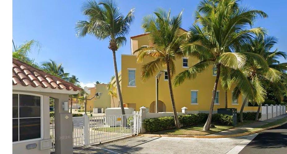 A yellow multi-story building stands behind a gated entrance with palm trees and landscaping — Harbour Drive Street PLAZA DEL PUERTO @ PALMAS DEL MAR DRIVE NE UNIT A-9, HUMACAO, PR